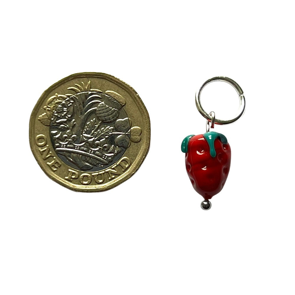 Glass strawberry bead hanging from a jump ring to create a stitch marker. Shown with a pound coin for scale.