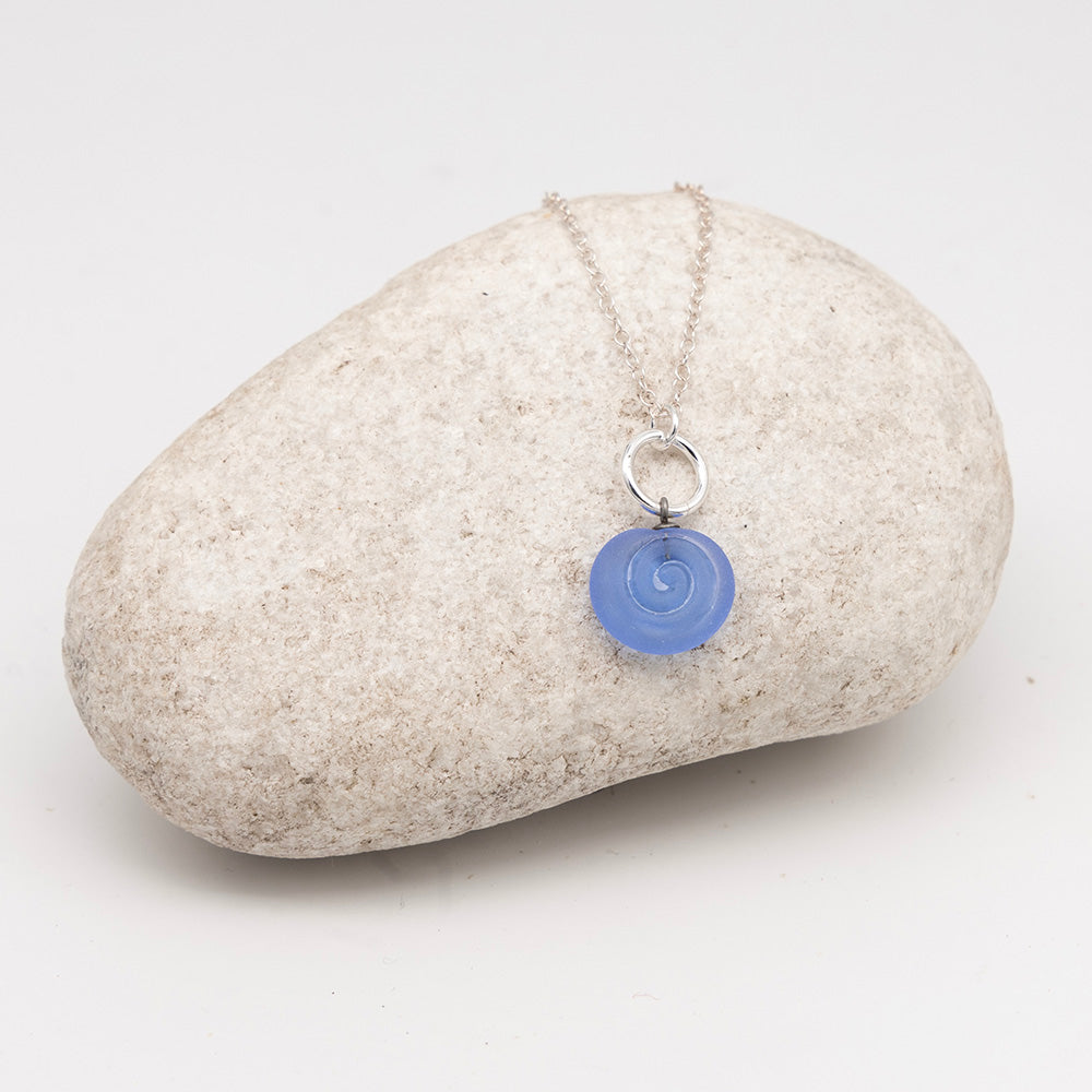 blue glass swirl charm necklace on a pale grey rock