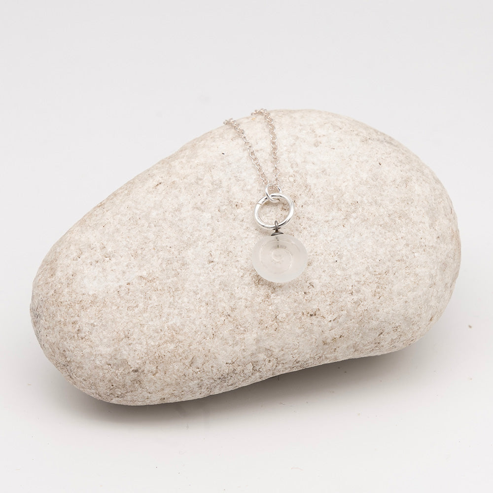 clear glass swirl charm necklace on a pale grey rock