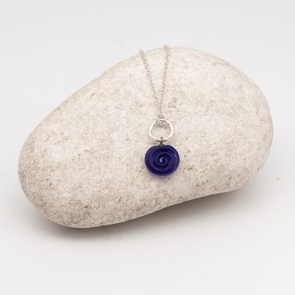 dark blue glass swirl charm necklace on a pale grey rock