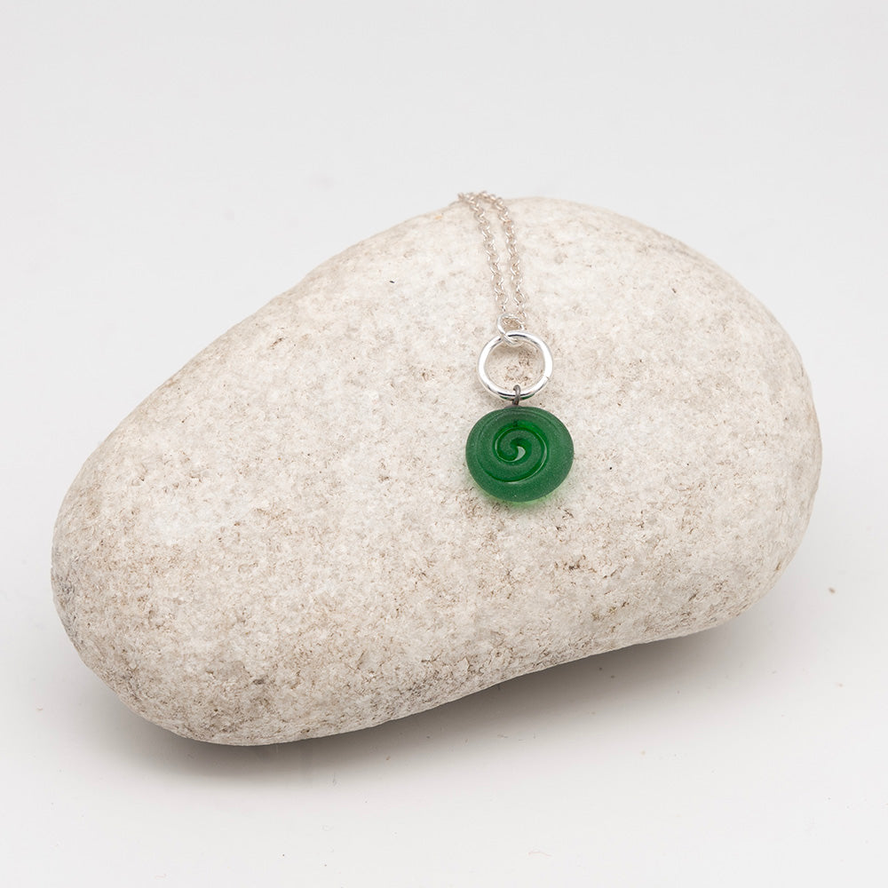 green glass swirl charm necklace on a pale grey rock