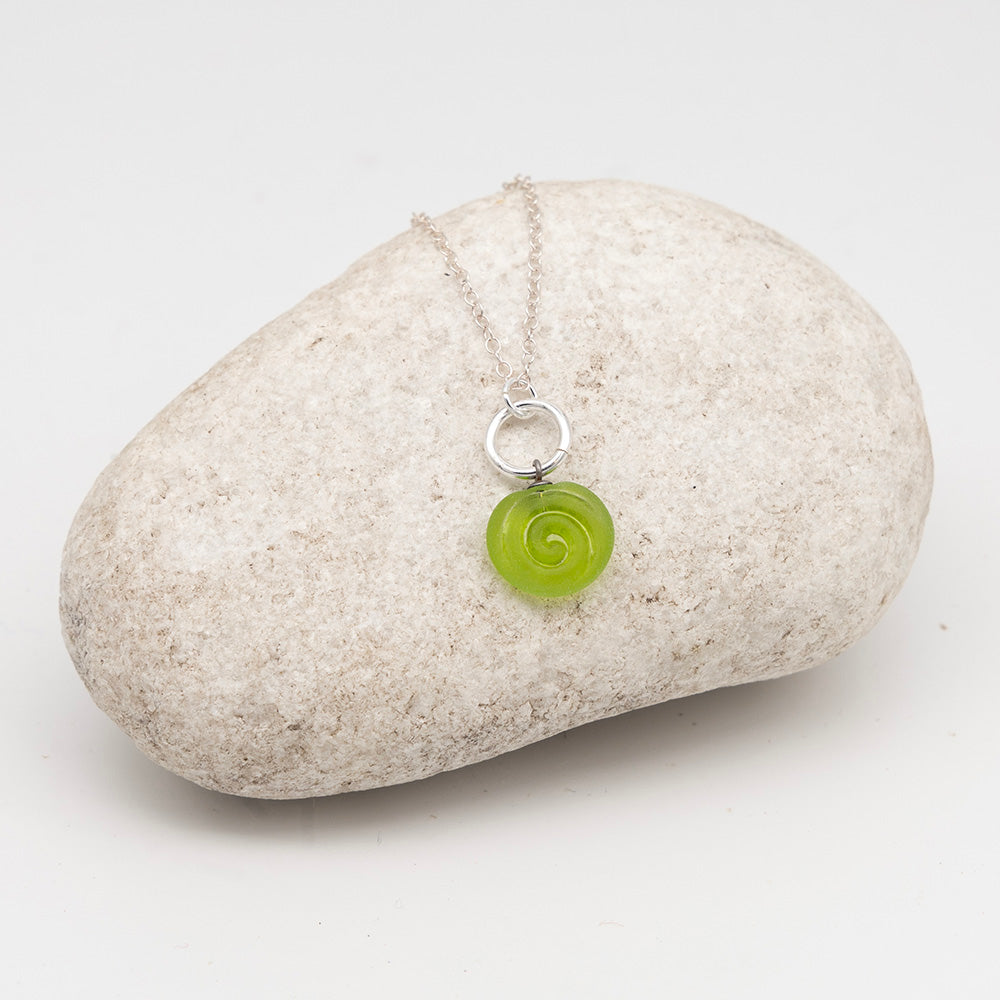 lime glass swirl charm necklace on a pale grey rock