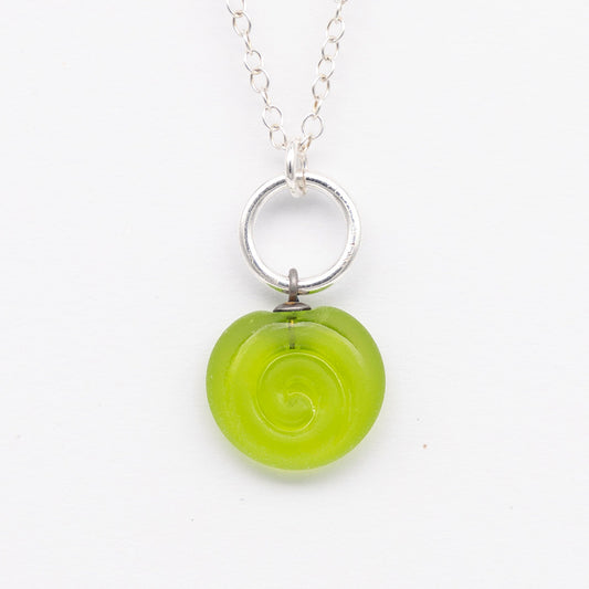 Close up of lime frosted glass charm with swirl imprint. The charm is frosted and spiral is shiny. The charm hangs on a large silver jump ring. The necklace is completed with a small silver jump ring and silver chain.