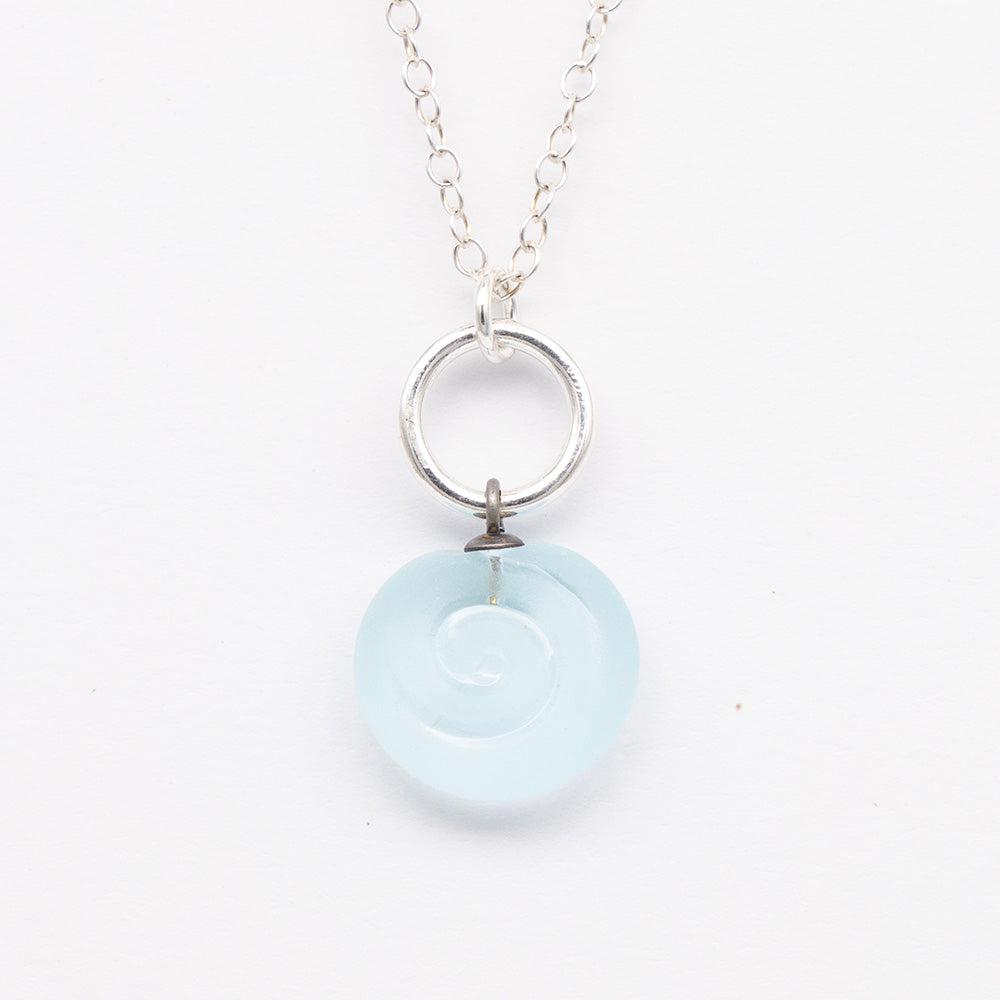 Close up of pale blue frosted glass charm with swirl imprint. The charm is frosted and spiral is shiny. The charm hangs on a large silver jump ring. The necklace is completed with a small silver jump ring and silver chain.