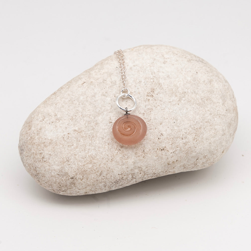 pink glass swirl charm necklace on a pale grey rock