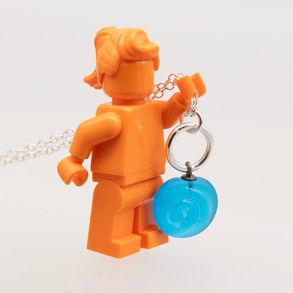 Swirl necklace held by orange lego mini figure to show scale. The glass charm is approximately the same height as the legs.