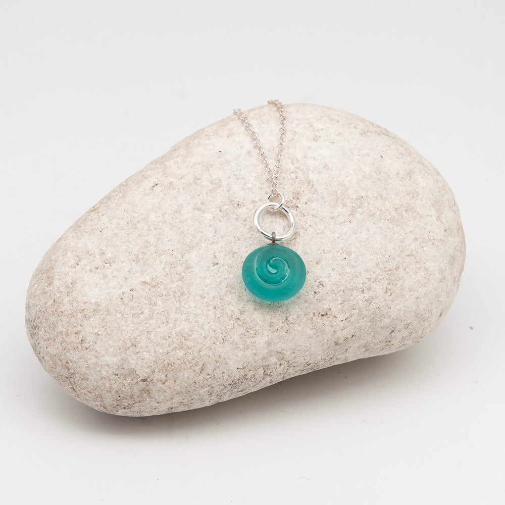 teal glass swirl charm necklace on a pale grey rock