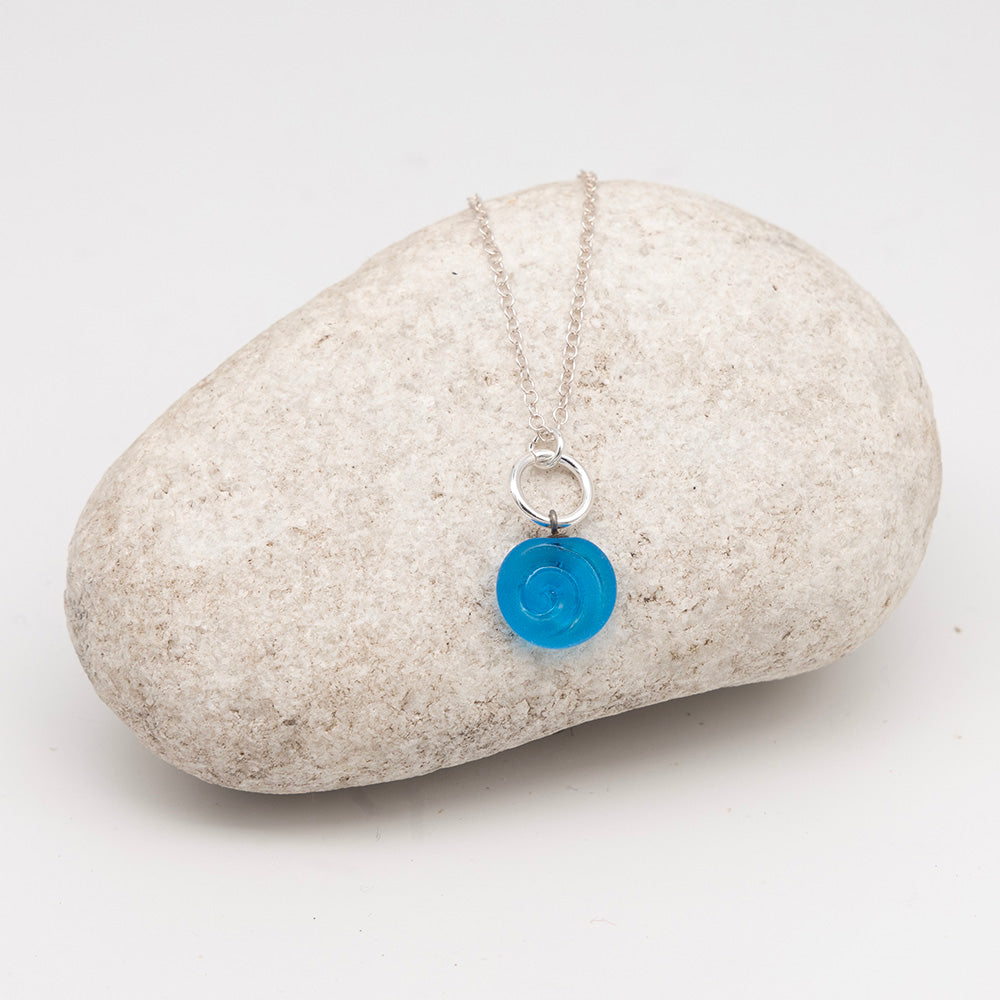 Turquoise glass swirl charm necklace on a pale grey rock