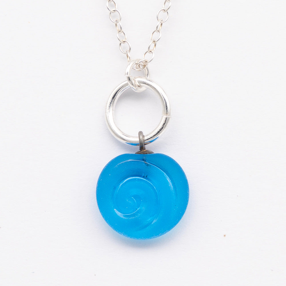 Close up of turquoise frosted glass charm with swirl imprint. The charm is frosted and spiral is shiny. The charm hangs on a large silver jump ring. The necklace is completed with a small silver jump ring and silver chain.