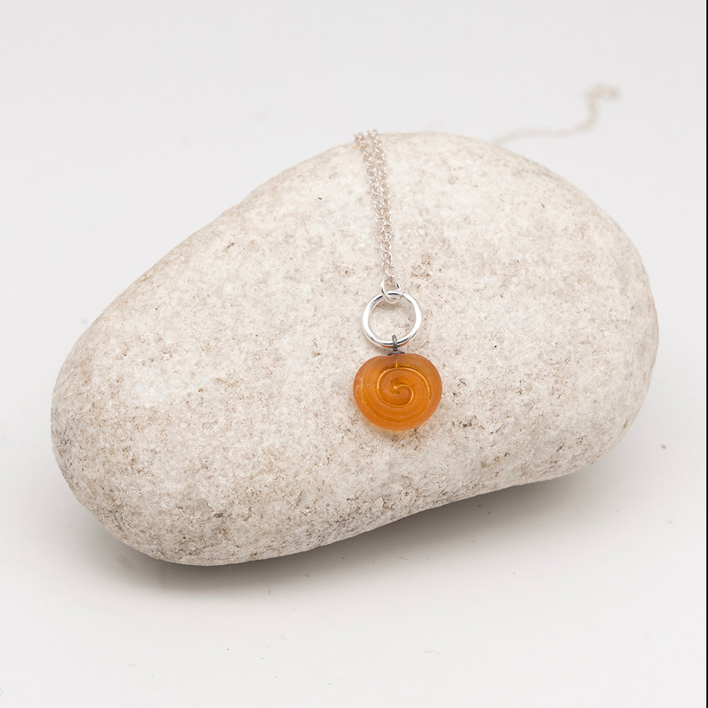 yellow glass swirl charm necklace on a pale grey rock