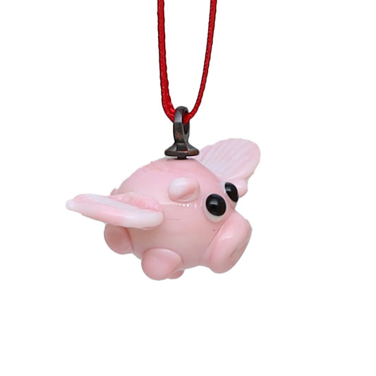 Tiny glass flying pig on a red ribbon. Pig is pale pink and has cartoon style eyes.