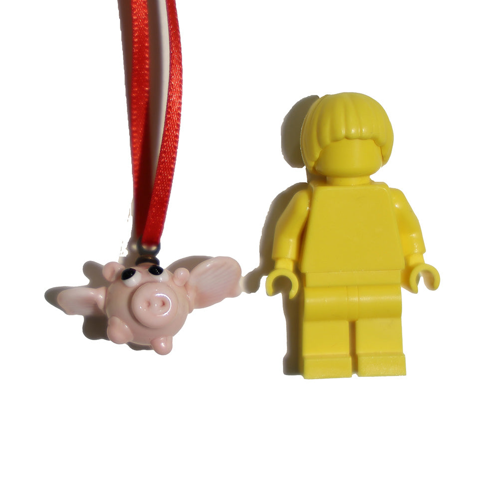 Tiny flying pig glass decoration shown with a lego figure for scale.