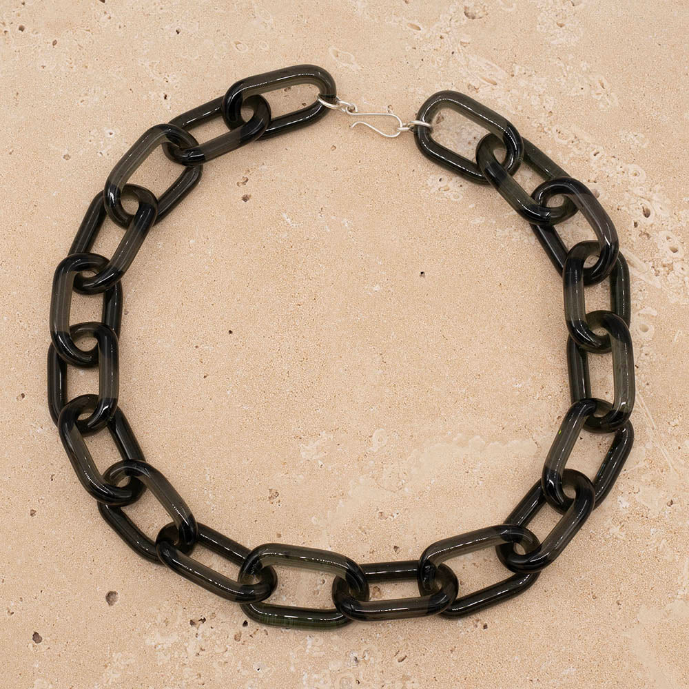 Chain link necklace made with transparent black glass. The necklace fastens with a sterling silver hook and eye. Photographed laid flat on a sandstone tile.