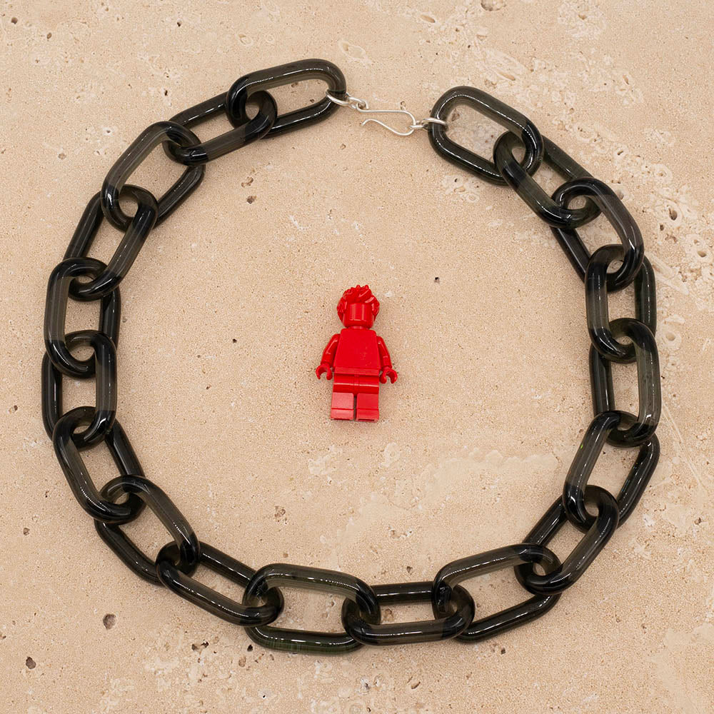 Necklace made with transparent black glass links. The necklace sits on a sandstone tile and is shown with a lego figure for scale.