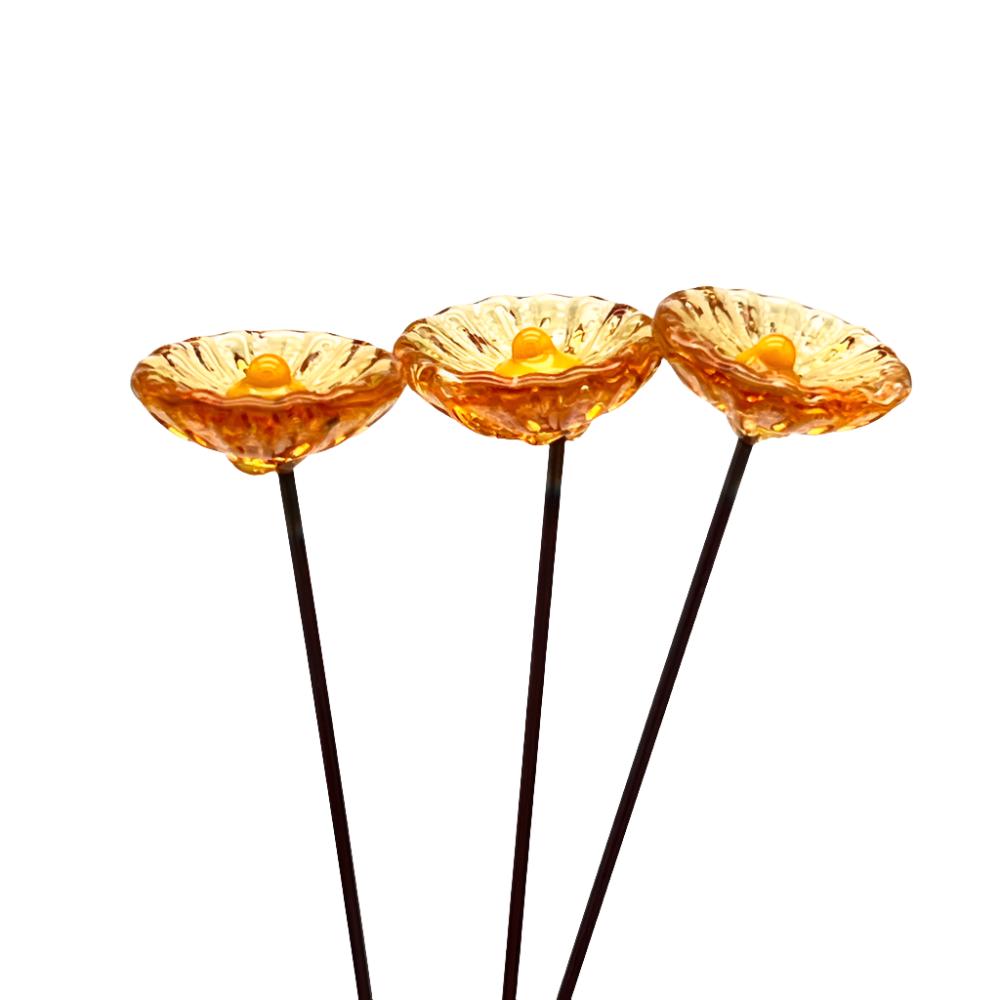 three transparent amber glass daisies with yellow centres on metal stakes