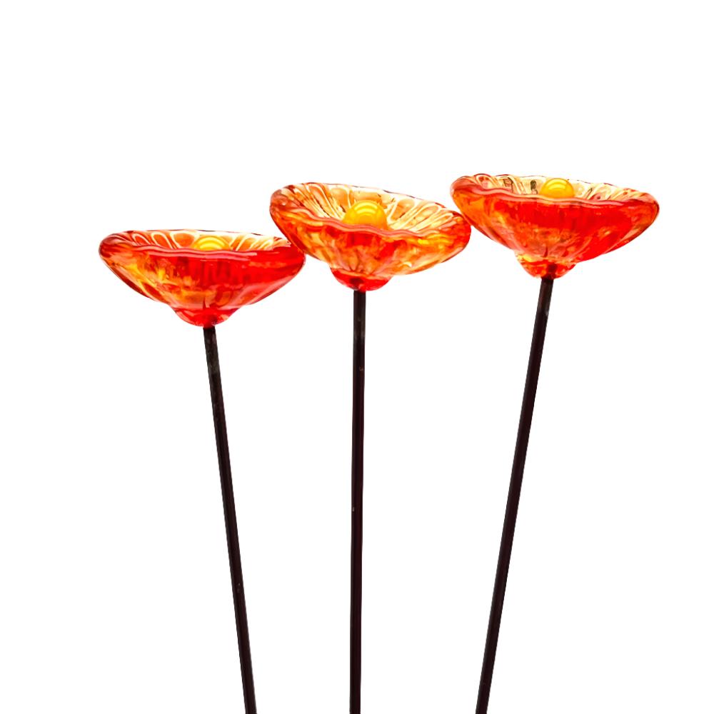 three transparent orange glass daisies with yellow centres on metal stakes