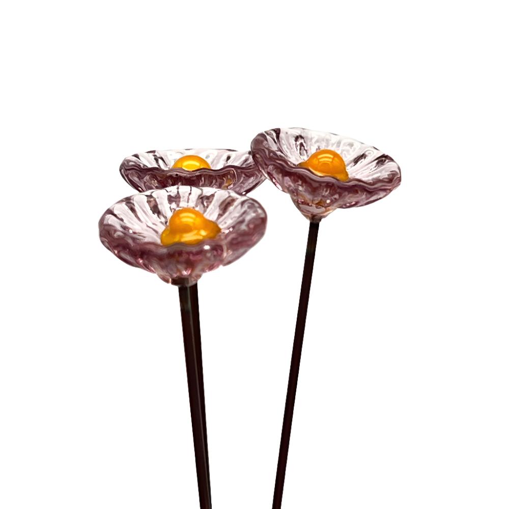 three transparent pink glass daisies with yellow centres on metal stakes