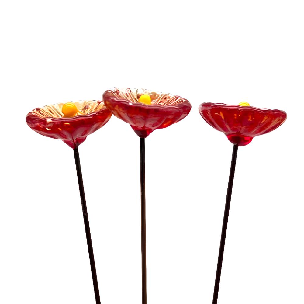 three transparent red glass daisies with yellow centres on metal stakes