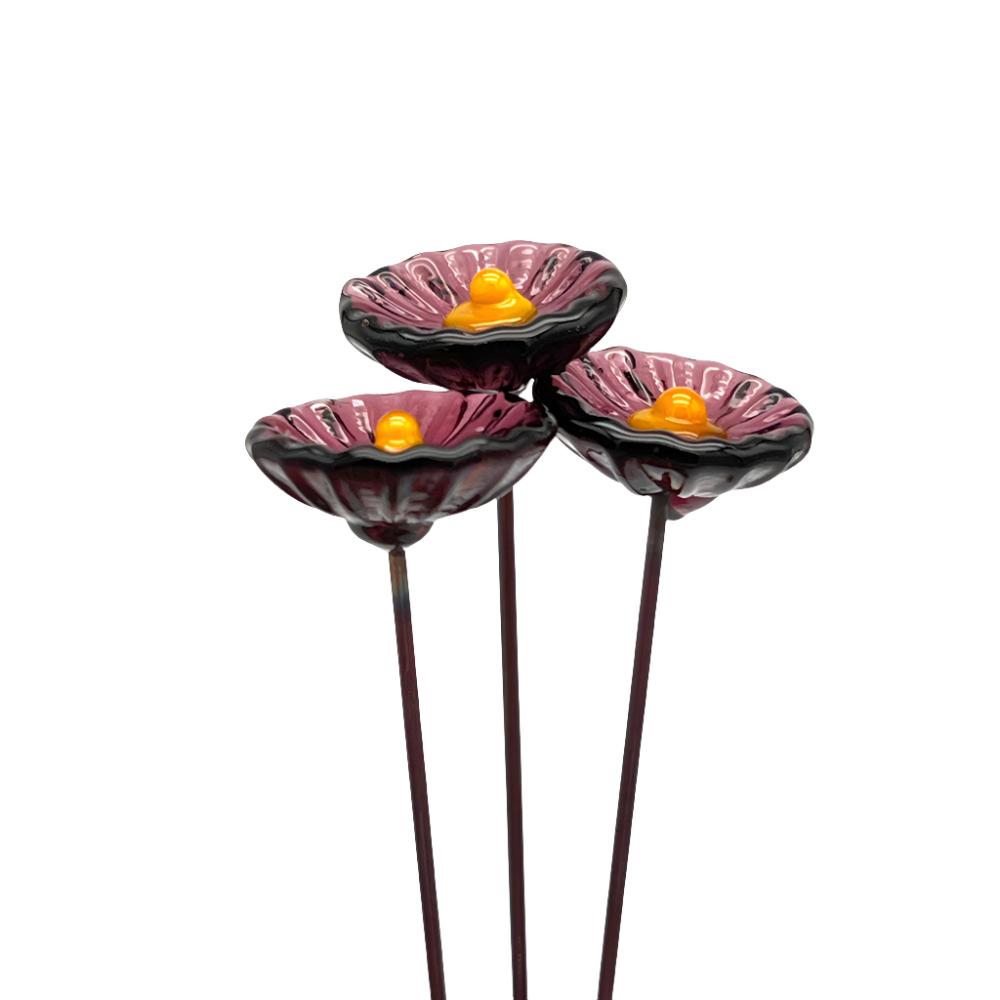 three transparent purple glass daisies with yellow centres on metal stakes