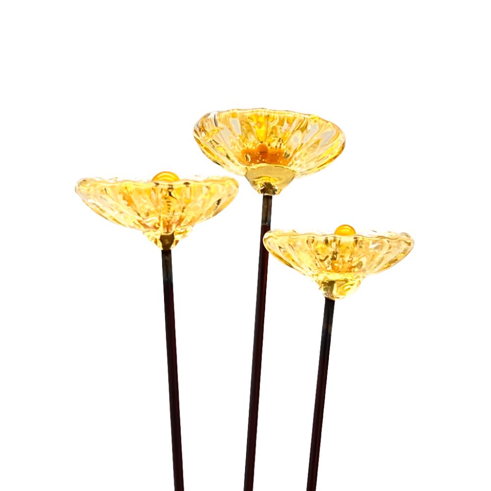 three transparent yellow glass daisies with yellow centres on metal stakes