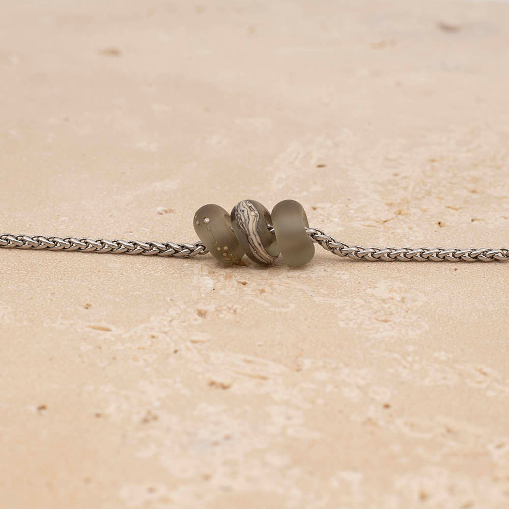 Three frosted grey glass beads on a stainless steel chain on a sandstone tile