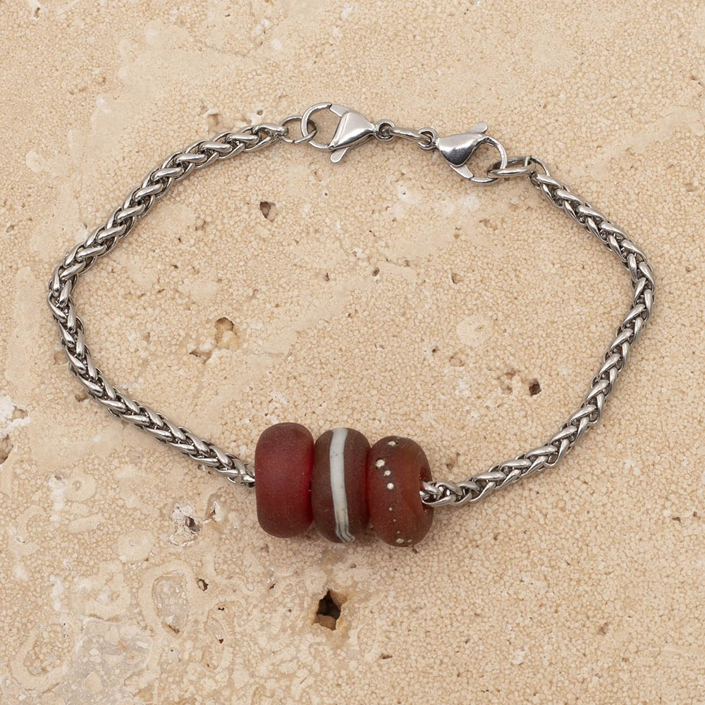 Three glass beads on a chain bracelet. The beads are made with deep pink glass. One is plain, one has a band of ivory glass and one has tiny dots of silver. All three beads have a frosted finish. The chain is a wheat chain so it has a pleated look. The bracelet fastens with a double lobster clasp.