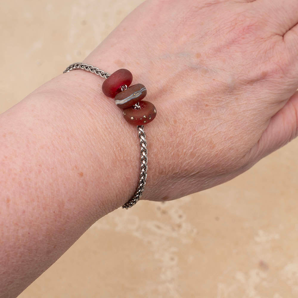 Three frosted pink glass beads on a stainless steel chain bracelet, shown on Joy's wrist