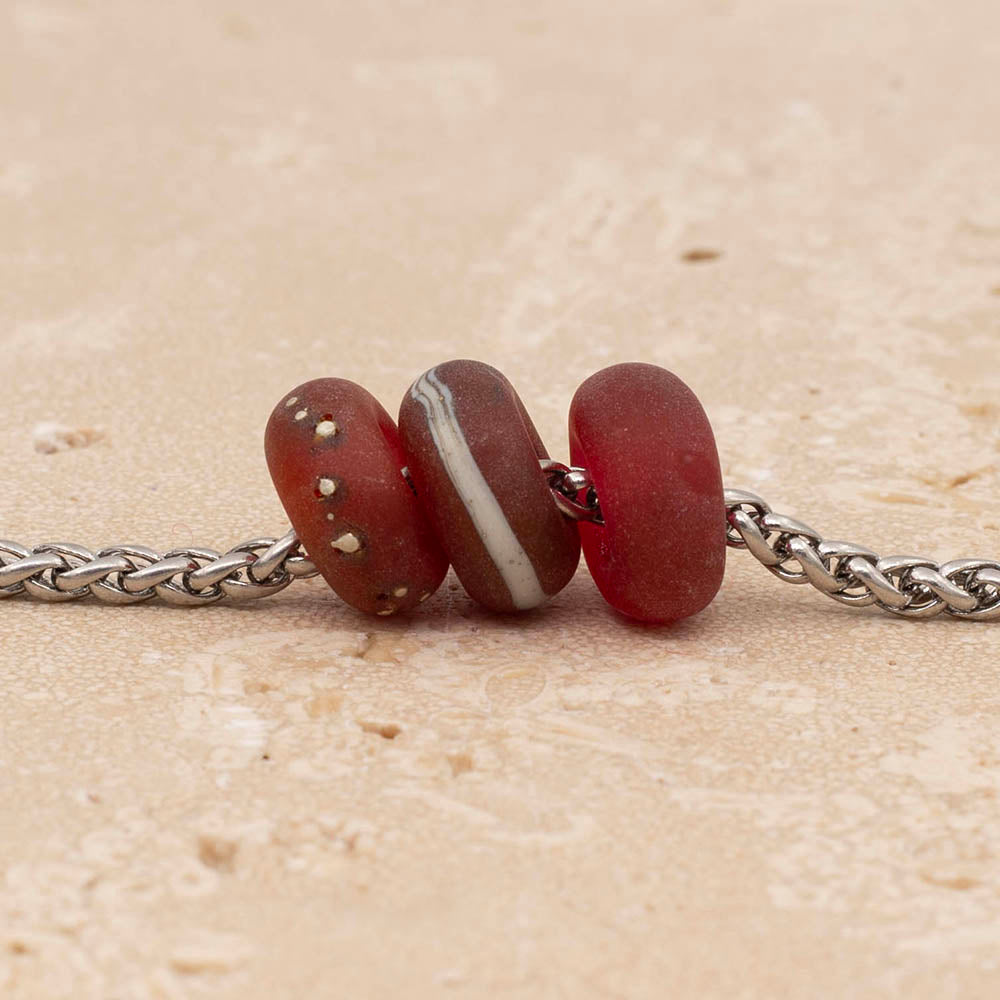 Close up of three frosted pink glass beads on a stainless steel chain