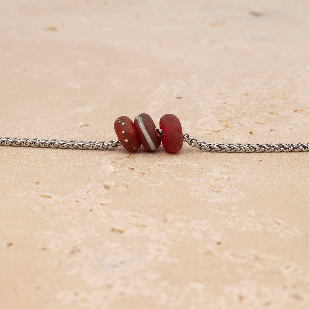 Three frosted pink glass beads on a stainless steel chain. The beads are plain, decorated with silver and decorated with ivory glass