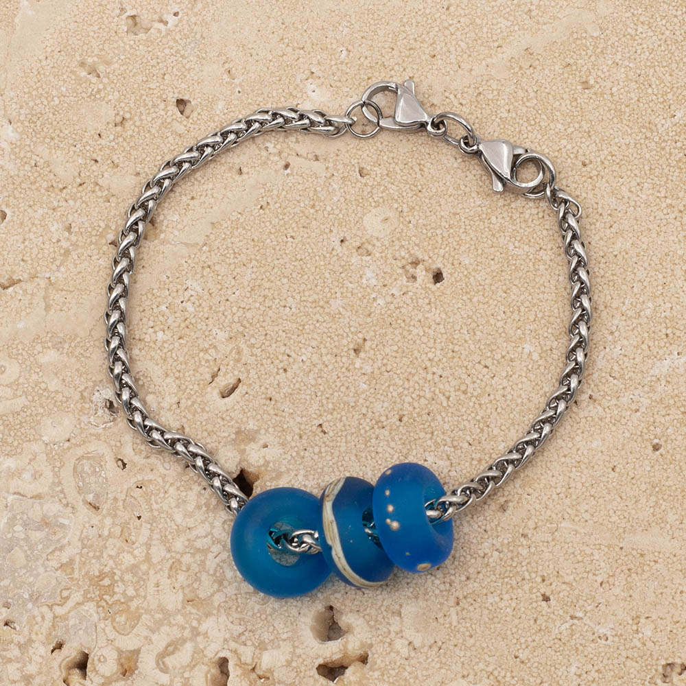 Three lampwork beads on a stainless steel chain bracelet. The beads are made with turquoise glass and have a frosted finish. One is plain, one has a band of ivory glass and one has dots of silver. The chain is a chunky wheat weave , so it looks pleated and it fastens with two lobster clasps.