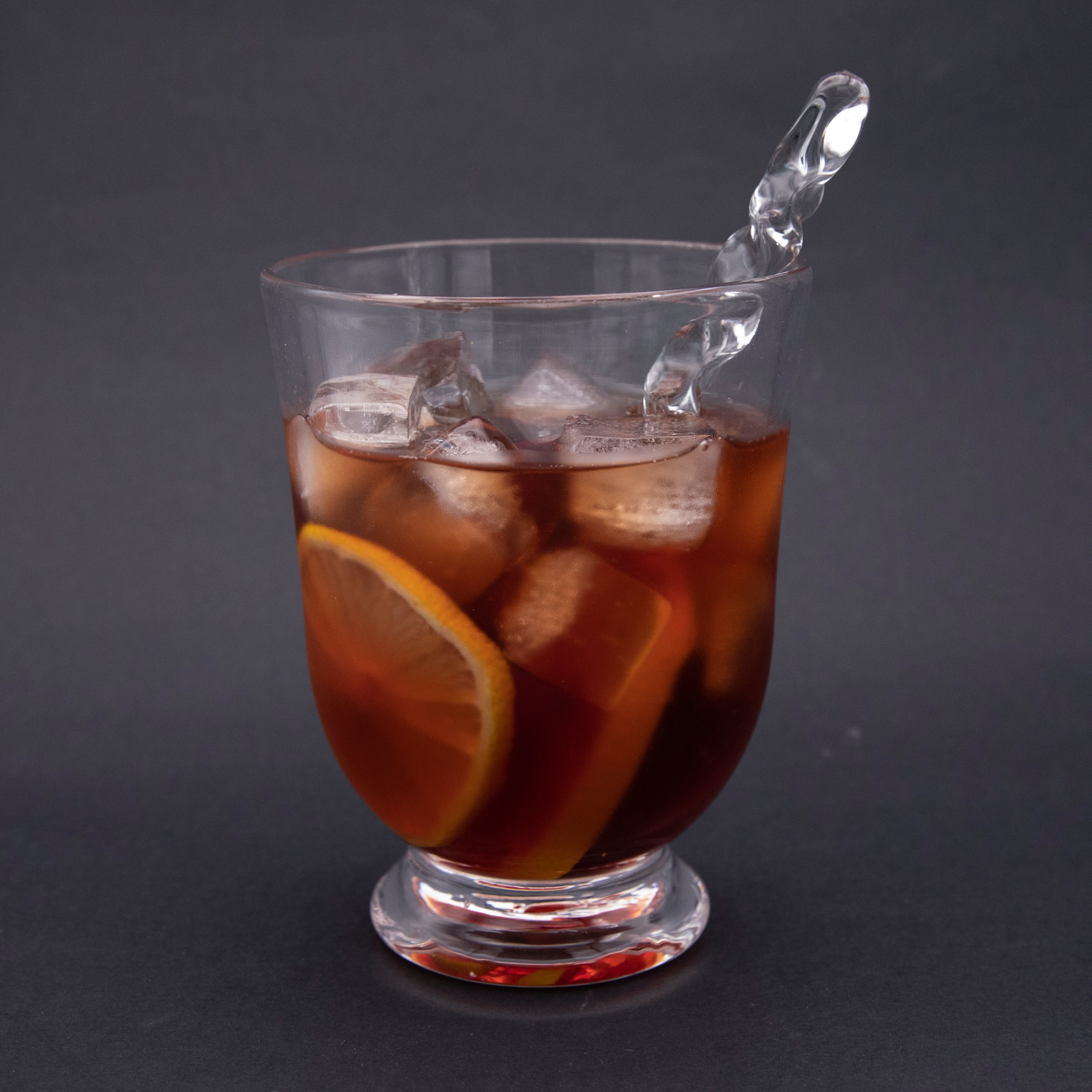 Clear zig zag cocktail stirrer in a tumbler filled with negroni cocktail,orange slices and ice